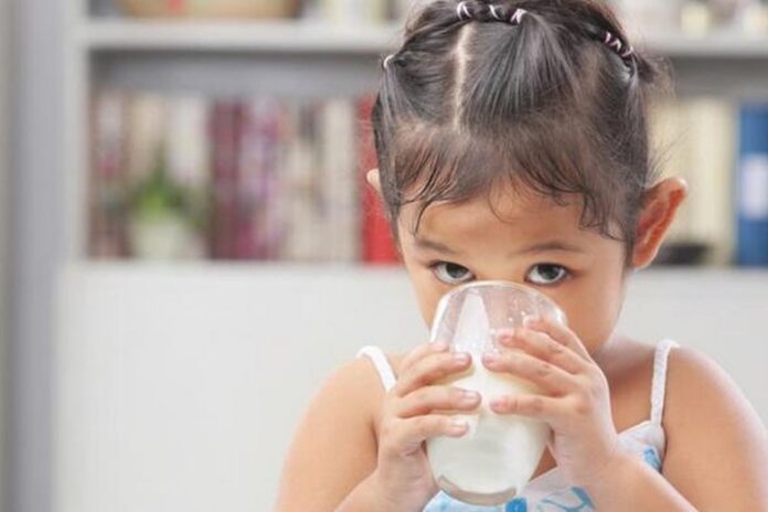 Gelas berisi susu sapi putih di atas meja kayu dengan latar belakang dapur yang cerah